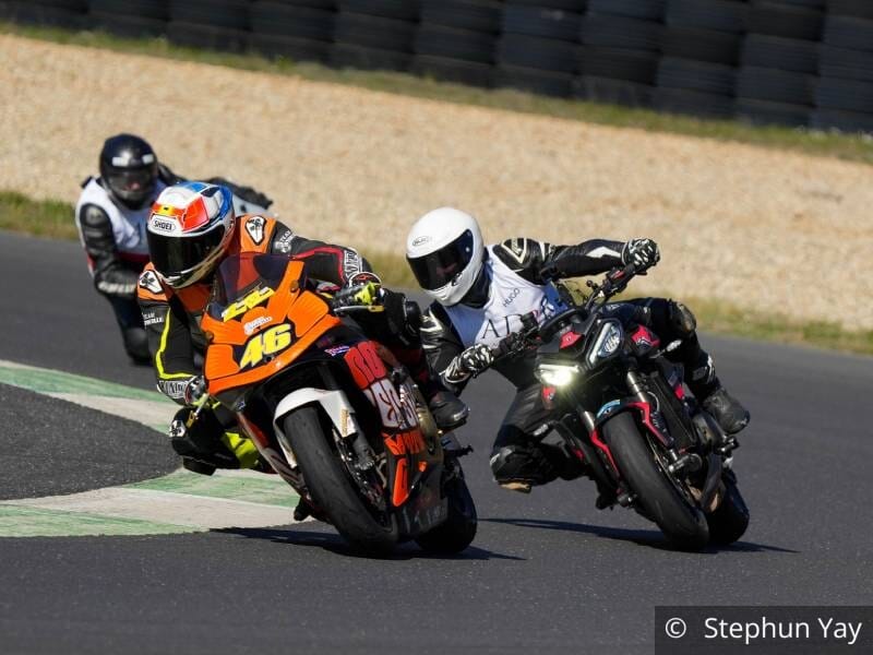 Trois pilotes de moto sur un circuit, dans un virage, deux au premier plan et un au second